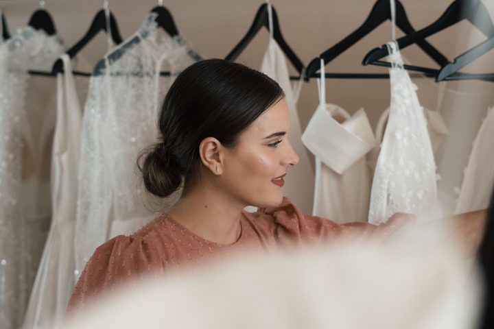 a woman standing near hanging wedding gowns Licensed inspiration image; not a BMG client portfolio claim.