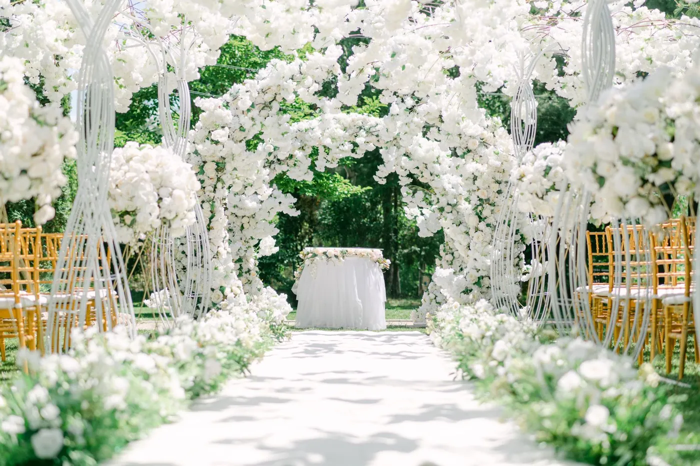 An elegant outdoor wedding venue setup with white floral arches and chairs. Licensed inspiration image; not a BMG client portfolio claim.