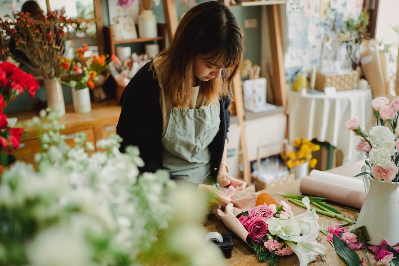 Concentrated young female florist in uniform standing near counter and arranging bouquet while working in light floral shop Licensed inspiration image; not a BMG client portfolio claim.