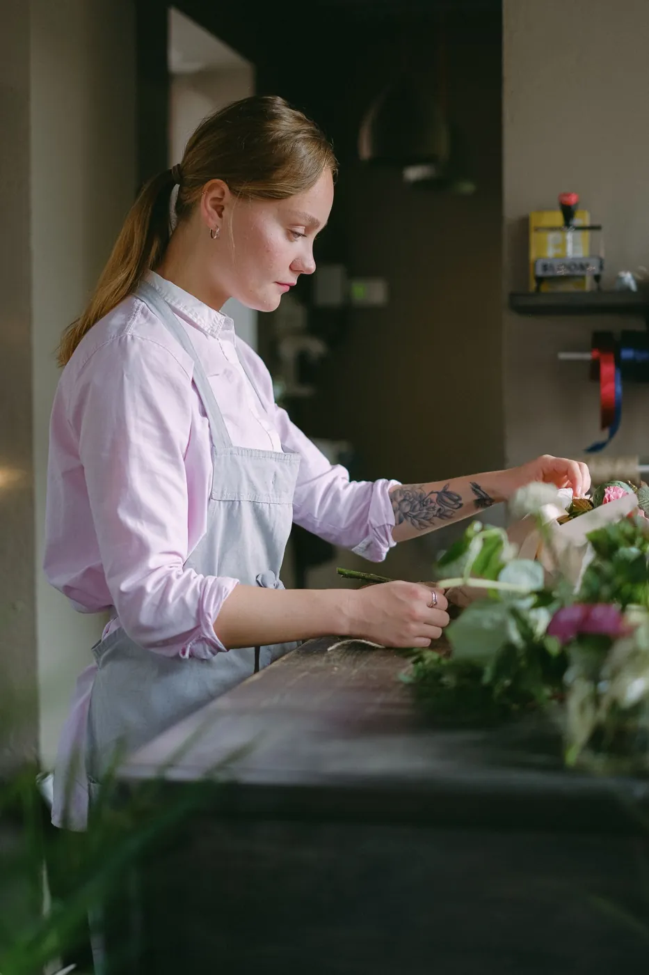 A female florist carefully arranges a bouquet in a cozy flower shop. Licensed inspiration image; not a BMG client portfolio claim.